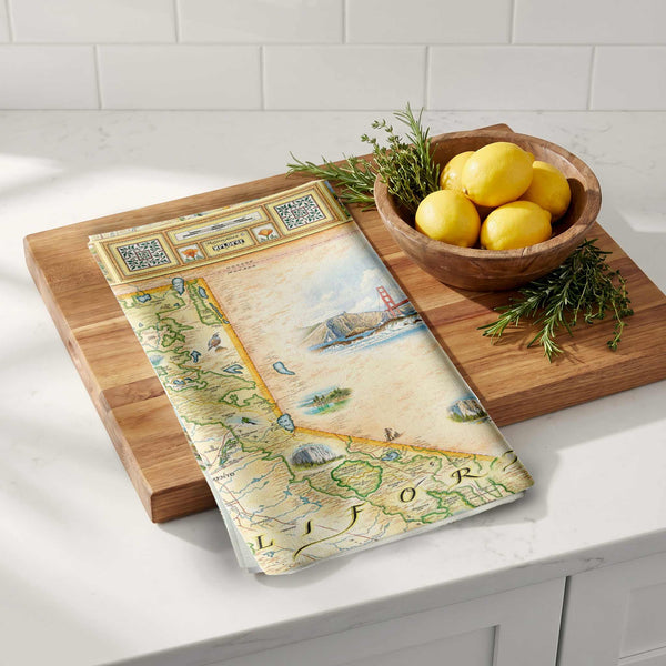 Wooden cutting board with map design on a kitchen counter, next to a bowl of lemons and herbs.
