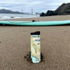 California Travel Drinkware sitting on the beach. In the background is a sea foam green surf board and the Golden Gate Bridge.