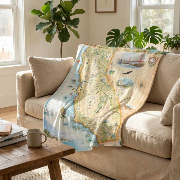 Beige sofa with a decorative blanket featuring a map design, in a room with plants and a coffee table.