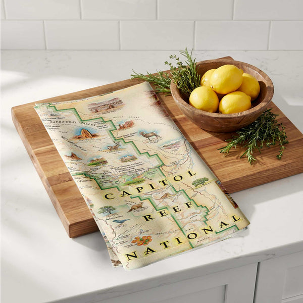 Wooden cutting board with a map-themed towel and a bowl of lemons on a kitchen counter.