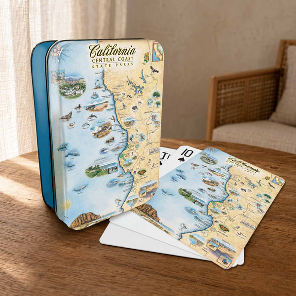 A California Central Coast State Parks themed playing set, featuring a decorative tin box and playing cards with an illustrated vintage map design, displayed on a wooden table in a warm, sunlit room.