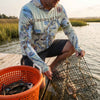 Person holding a crab trap with a Chesapeake Bay-themed Sun shirt hoodie  by a body of water.