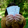 A person holding five Chesapeake Bay playing cards in front of their face. Park Like background. 