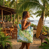 Woman holding a tote bag with a map design on a tropical beach.