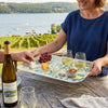 Woman holding a Finger Lakes tray with wine, cheese, and grapes by a scenic vineyard.