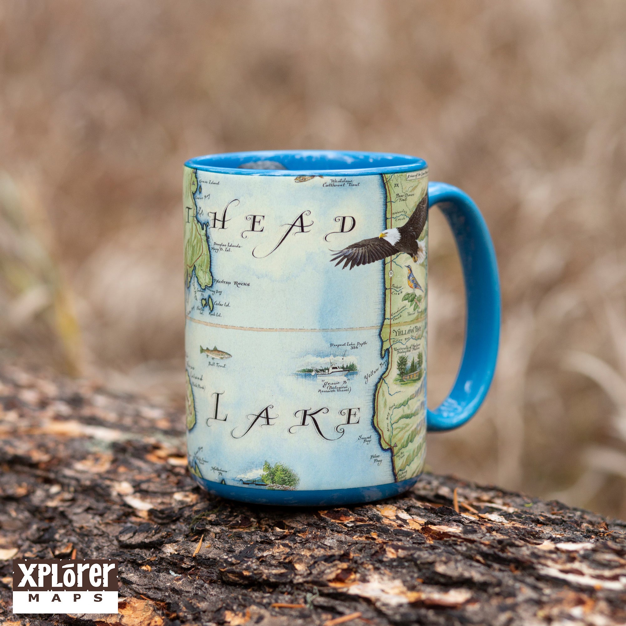 Blue 16 oz Montana's Flathead Lake Coffee Mug sitting on a log in the forest. 