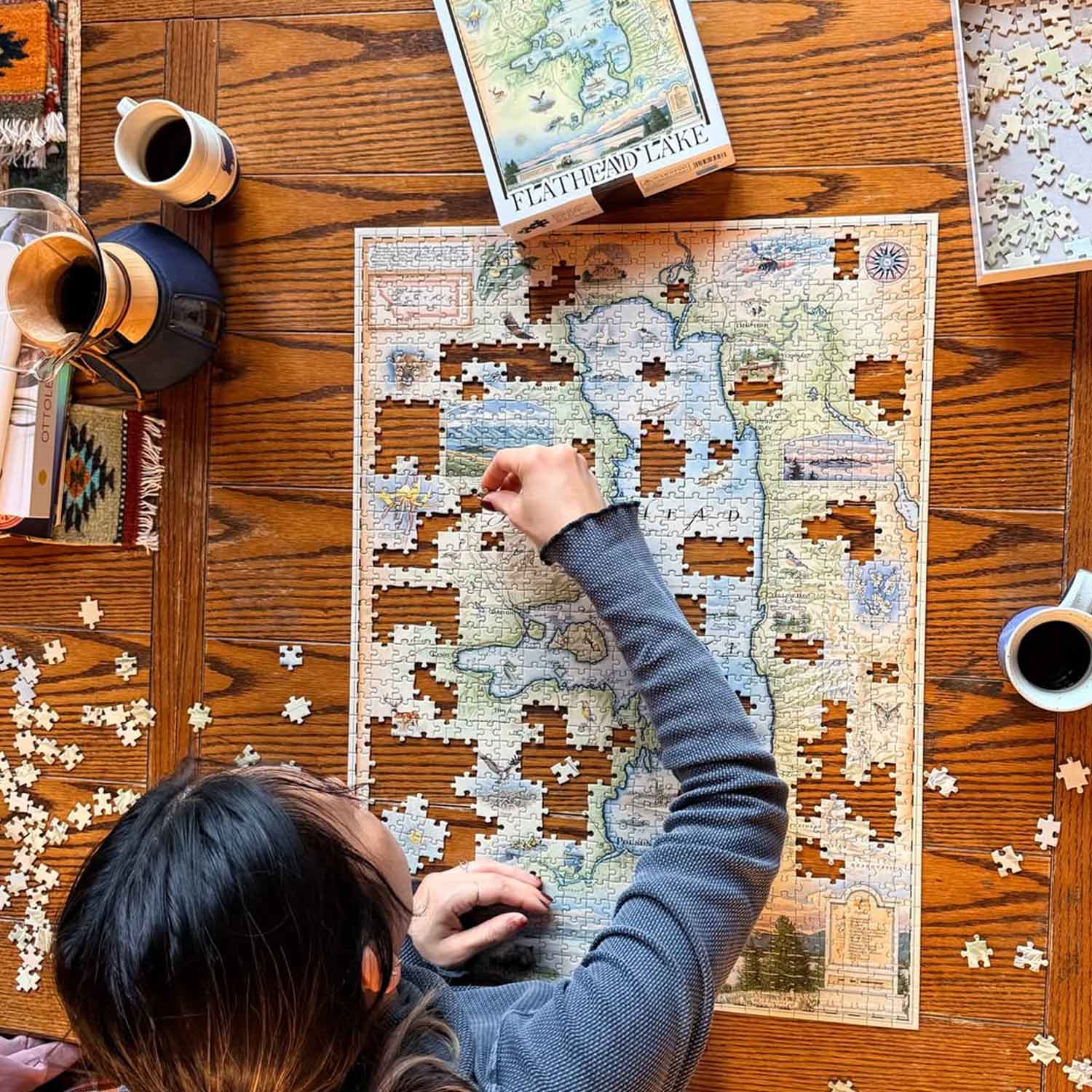 Person working on a puzzle of a map on a wooden table with coffee and books.