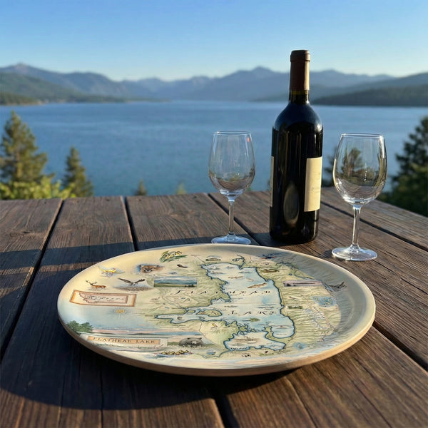 Wine bottle and glasses on a scenic lakeside table with a Flathead Lake map serving tray.
