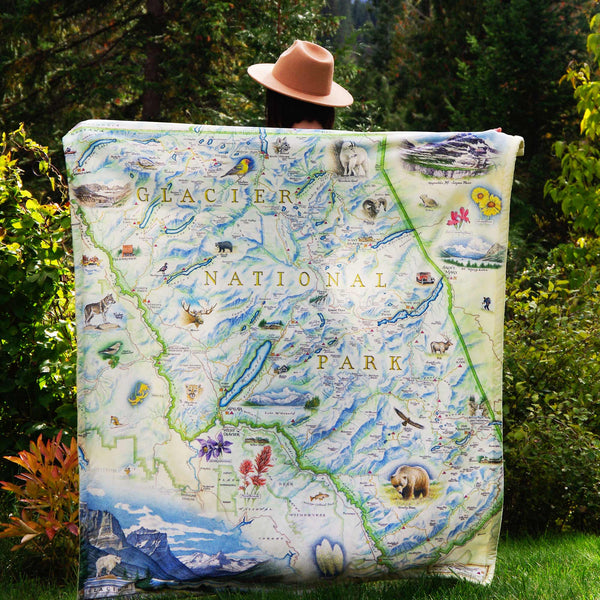 Person holding a  blanket with the map of Glacier National Park on it with nature-themed illustrations.