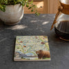 A square ceramic coaster featuring a vintage-style illustrated map of Yellowstone National Park with a grizzly bear at the bottom, displayed on a dark gray stone countertop next to a coffee maker and a potted plant.