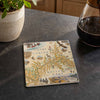 A square ceramic coaster featuring a vintage-style map illustration of Grand Canyon National Park, displayed on a dark gray kitchen countertop next to a potted plant and a coffee pot.