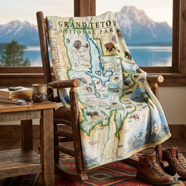 Map blanket of Grand Teton National Park draped over a wooden chair with a scenic view outside.