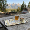 Camping scene with a glass of beer on a Grand Teton map tray, surrounded by nature.