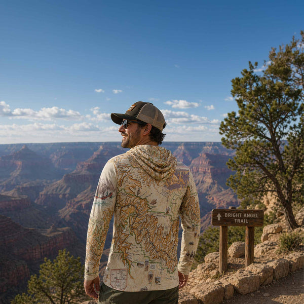 Person wearing a map-patterned hoodie overlooking the Grand Canyon with a 'Bright Angel Trail' sign.