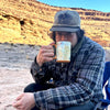 Grand Man drinking out of a Canyon National Park Map Coffee Mug in front of Grand Canyon. 