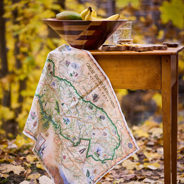 Map-themed towel draped over a wooden table with a bowl of fruit in an autumn setting