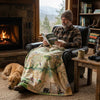 Man reading a book in a cozy living room with a fireplace and a dog lying on the floor. He has a Great Smokies blanket on him.