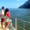 Two people standing on a boat deck overlooking a scenic ocean view with mountains.