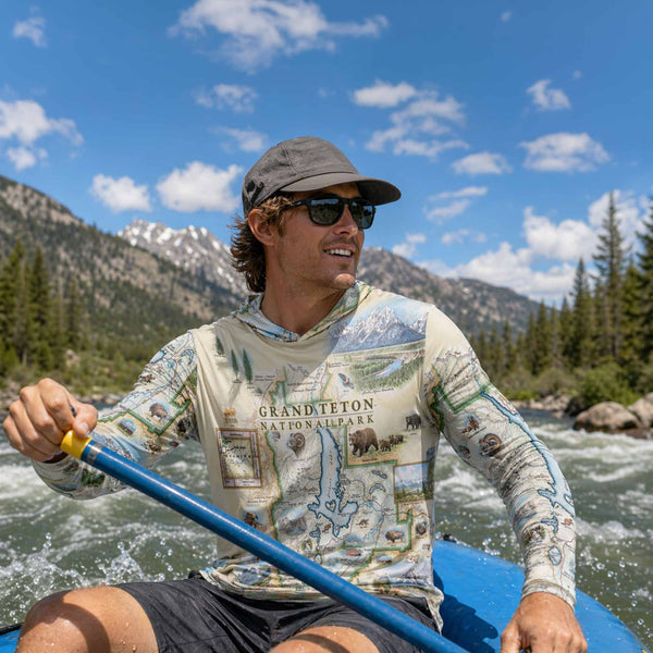 Man paddling a kayak in a mountainous area wearing a Grand Teton National Park sunshirt.