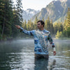Man fly fishing in a mountainous lake wearing a Alaska Inside Passage Sun Shirt Hoodie