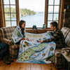Two people sitting in a cabin with a large Isle Royale National Park map draped over them, looking out at a lake.