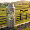 Stainless steel water bottle with Kentucky-themed label on a wooden post with a scenic background of horses in a field.