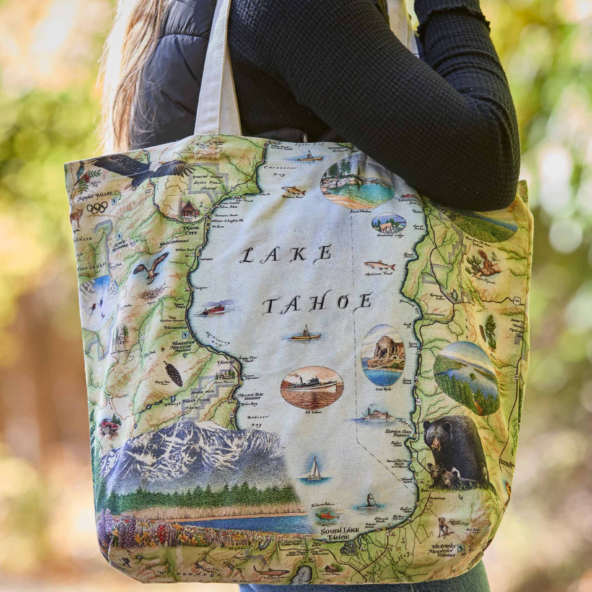 Tote bag with a map design of Lake Tahoe held by a person outdoors.
