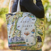 Tote bag with a map design of Lake Tahoe held by a person outdoors.