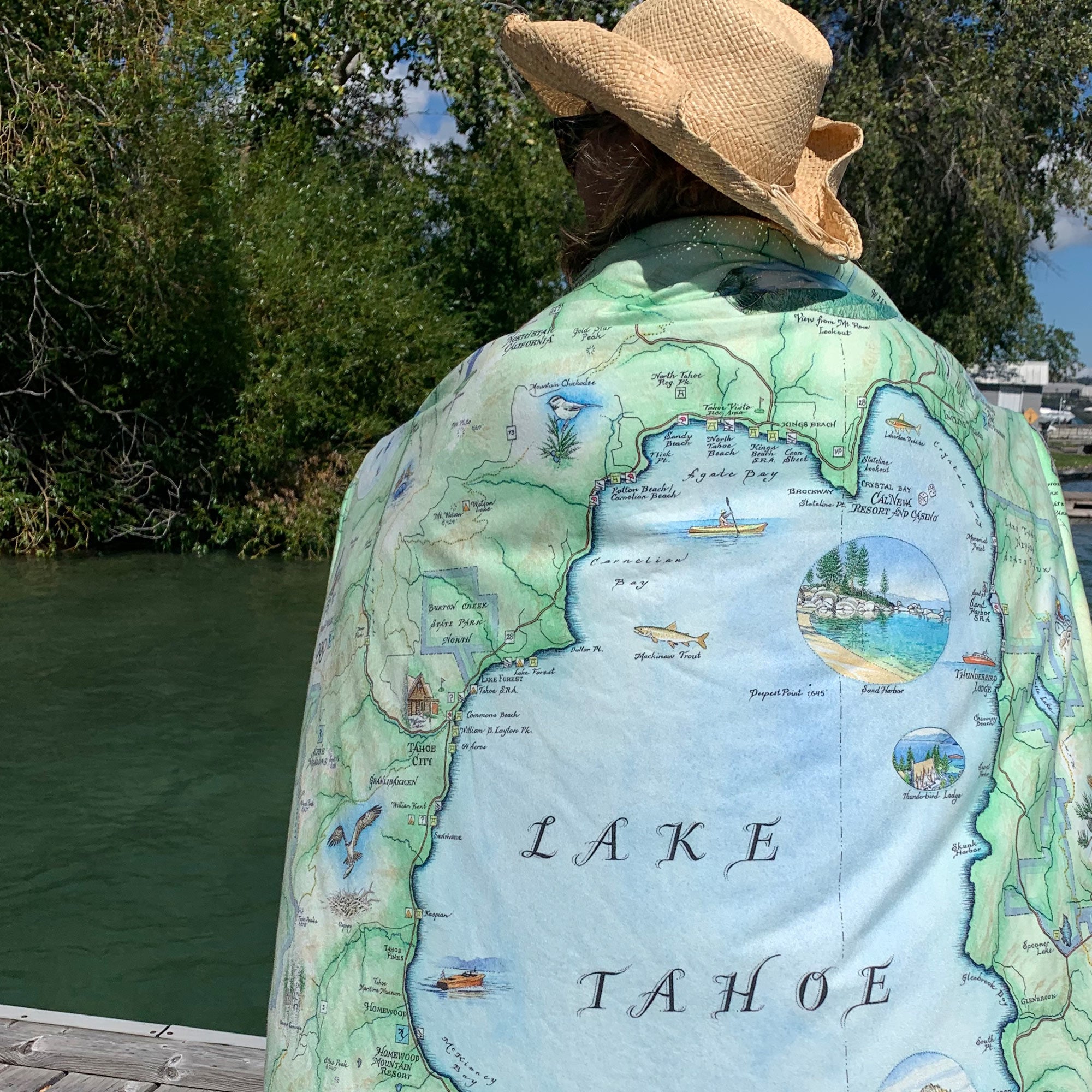 Person wearing a map of Lake Tahoe draped over their shoulders by a body of water.
