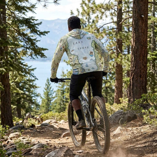 Person wearing a Tahoe sun shirt hoodie riding a bike on a trail with a scenic Lake Tahoe background