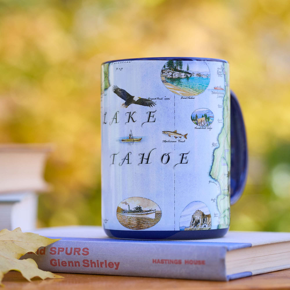 Mug with Lake Tahoe design on a book against a blurred natural background