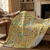 Person holding a book with a London map blanket draped over a couch.