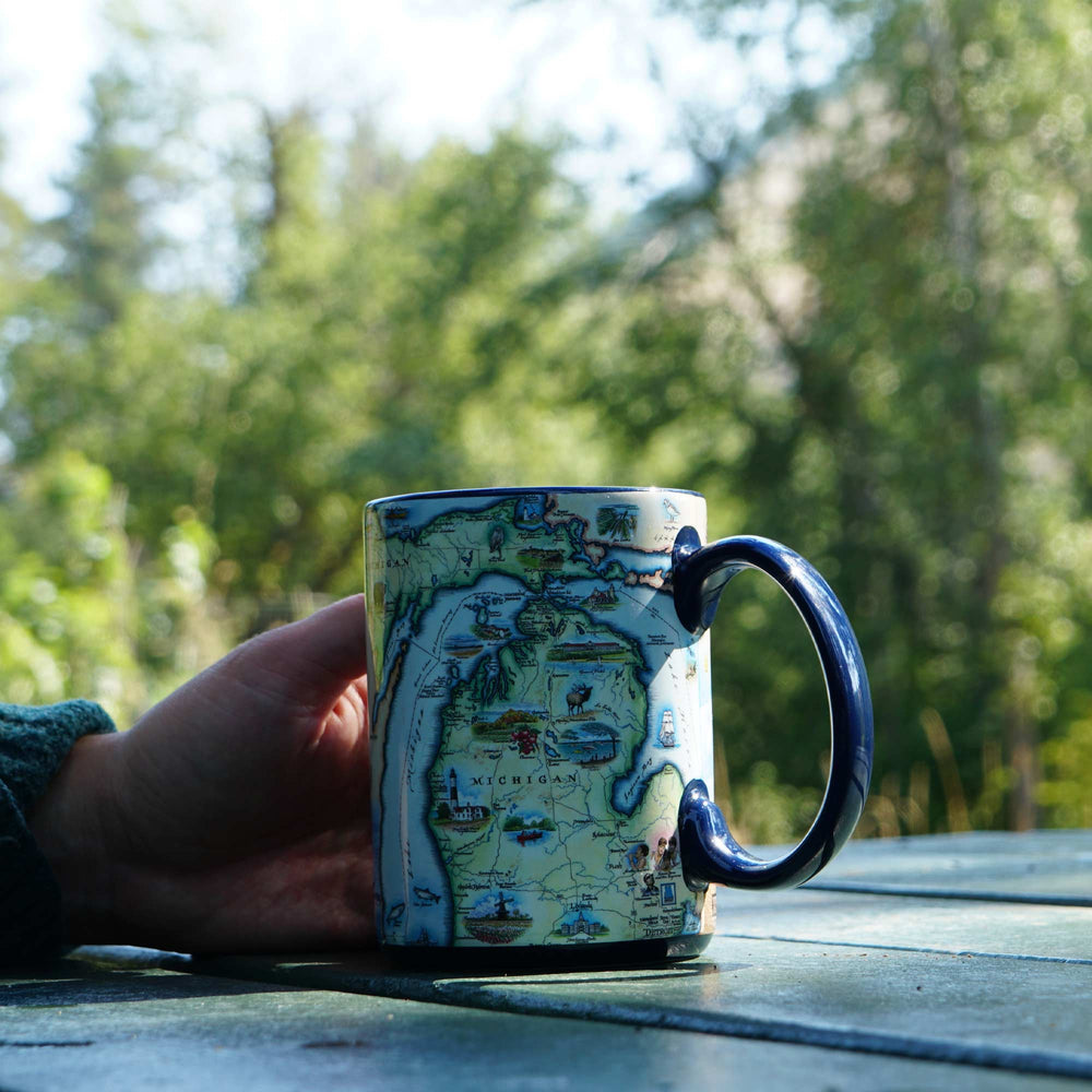 Person holding a mug with a map design of Michigan outdoors