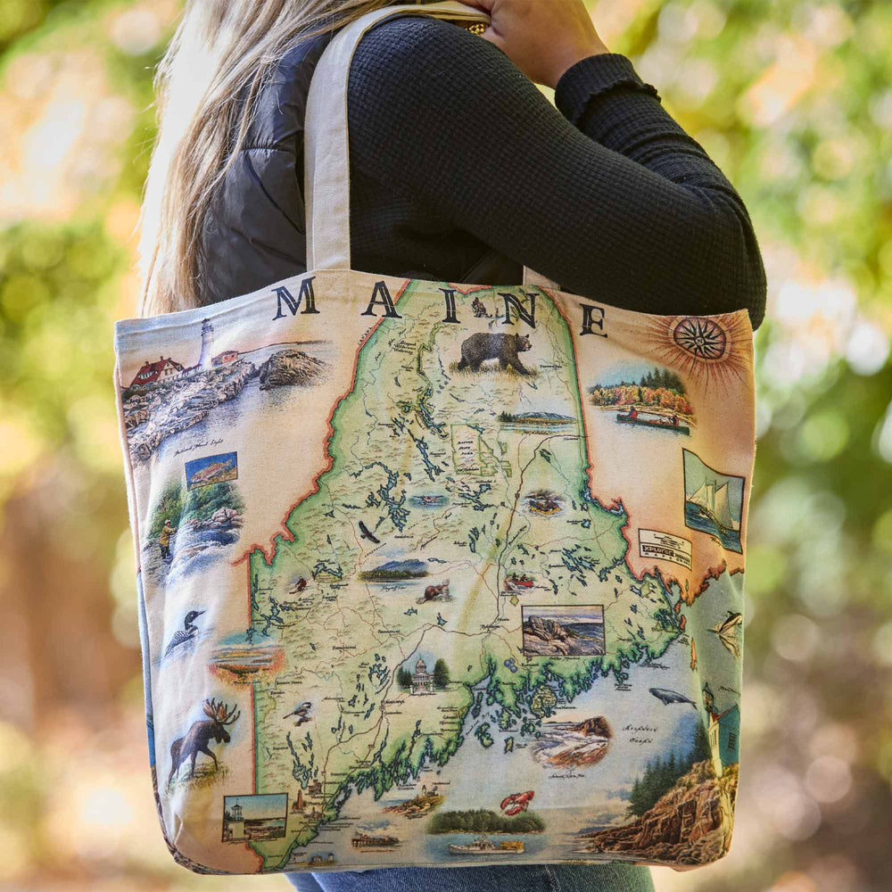 Tote bag with a map of Maine design held by a person outdoors.