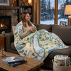 Woman sitting on a couch with a Michigan map-themed blanket, holding a mug in a cozy living room.
