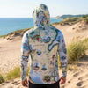 Person wearing a sun shirt hoodie with a map design standing on a sandy beach.