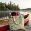 Tote bag with Minnesota-themed design on a dock by a lake with a canoe and camping supplies.