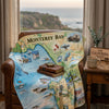 Map-themed blanket with 'Monterey Bay' printed on it draped over a chair in a room with a scenic view.