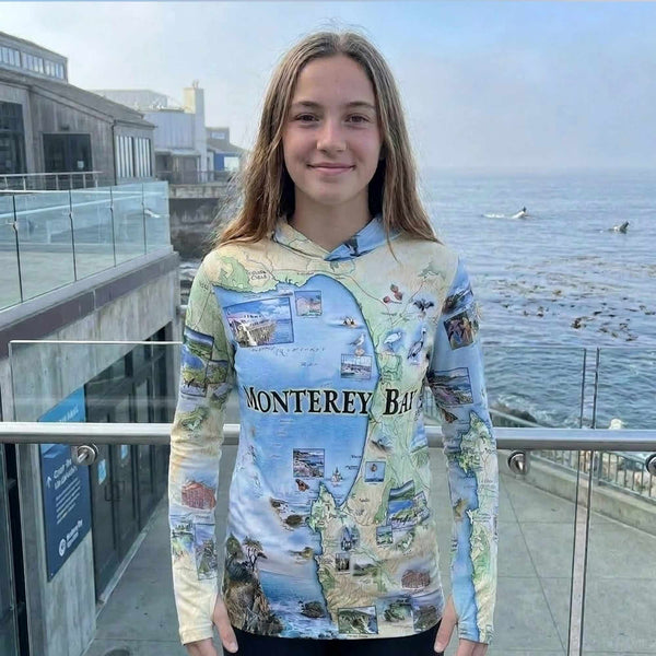 Person wearing a sun hoodie with Monterey Bay design by the ocean.