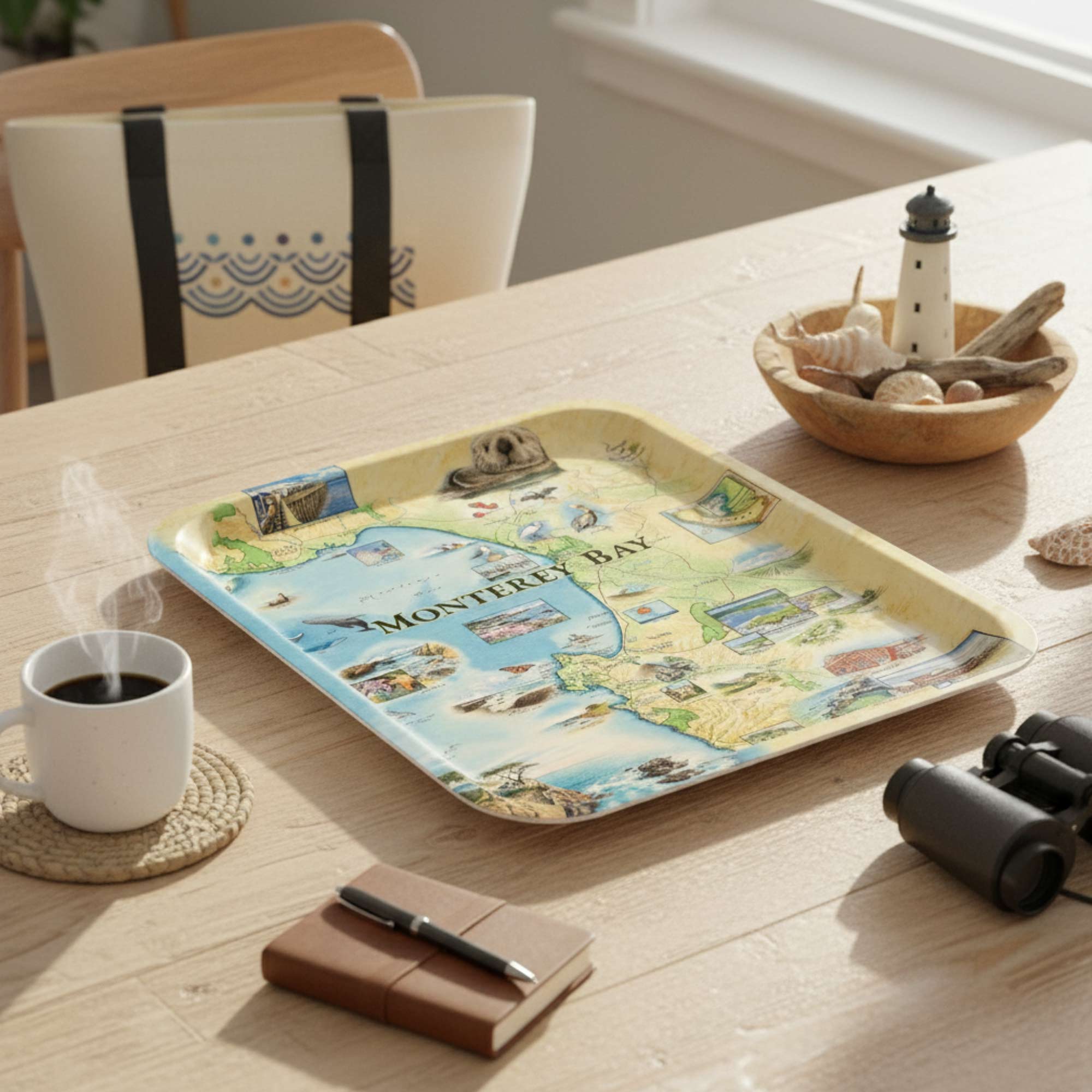 Monterey Bay  tray with a map design on a wooden table with a cup of coffee, notebook, and binoculars.