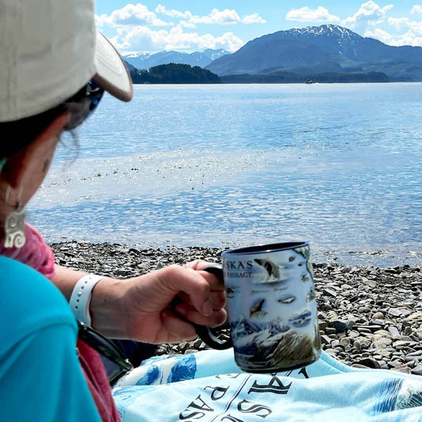 A Women in Icy Straights Alaska holding an Inside Passage mug on a rocky beach. 