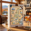 A 1000-piece New Hampshire jigsaw puzzle box displayed on a wooden table in a cozy, wood-paneled living room with a fireplace and window view of mountains and autumn foliage.
