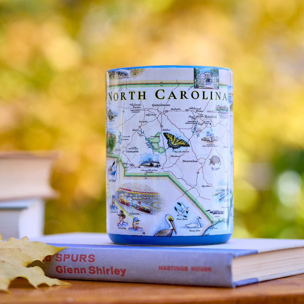 Ceramic mug with North Carolina map design on a book against a blurred natural background