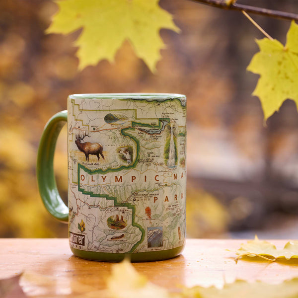 Mug with Olympic National Park design on a wooden surface with autumn leaves.