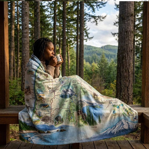 Person sitting on a wooden deck with a scenic blanket, surrounded by trees.
