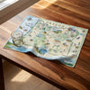 Oregon-themed dish towel on a wooden table with a glass of water.