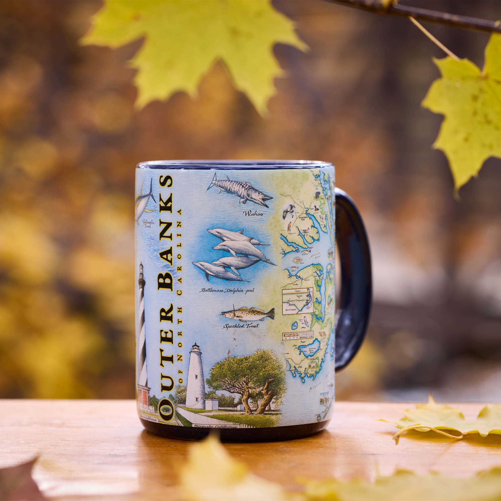 Mug with Outer Banks, North Carolina design on a wooden surface with autumn leaves.