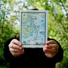 A women holding an Outer Banks blank notecard, showcasing intricate hand-drawn map artwork by Xplorer Maps artist Chris Robitaille.