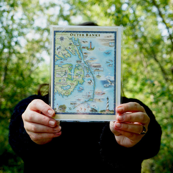 A women holding an Outer Banks blank notecard, showcasing intricate hand-drawn map artwork by Xplorer Maps artist Chris Robitaille.