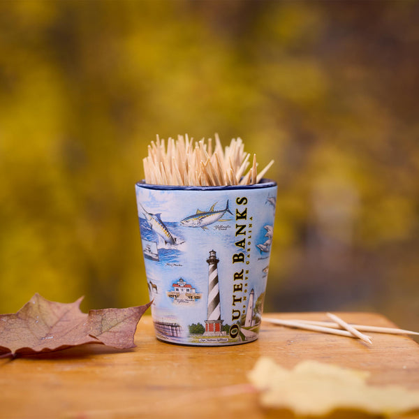 Shot glass of toothpicks with Outer Banks design on a wooden surface with blurred natural background